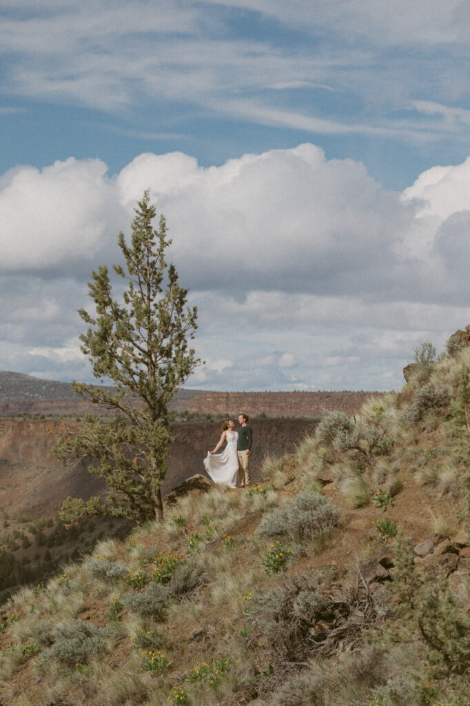 A pulled back photo showing a very small man and woman off in the distance on the Tam-a-lau Trail at Cove Palisades State Park in Oregon. The woman has thrown her white dress back so it flows out behind her.
