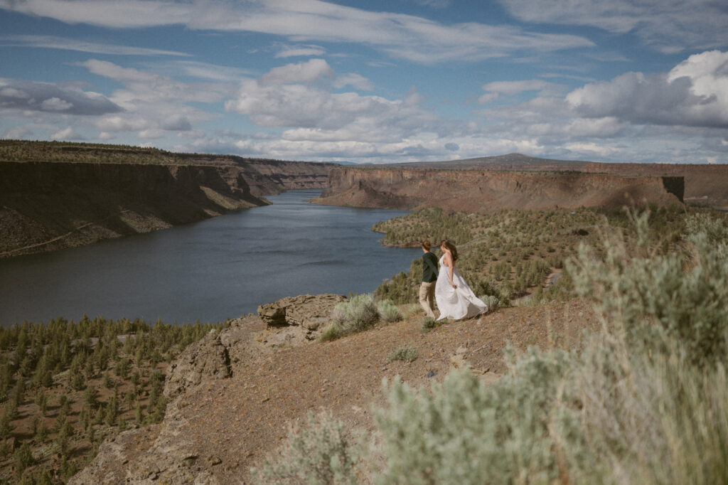 A man leads a woman down the Tam-a-lau Trail at Cove Palisades State Park. It's a bright sunny day and the river canyon streches out into the horizon behind them.