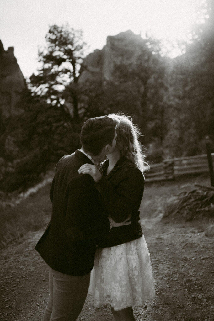 A black and white image of two woman kissing at Smith Rock in Terrebonne, Oregon. The first woman has her hands on the second woman's hips as she leans in and kisses her cheek.
