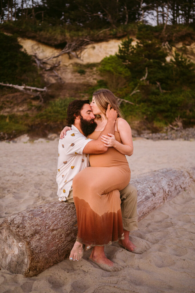 A young couple embraces on a log during their maternity session at Seal Rock Beach in Seal Rock, Oregon.