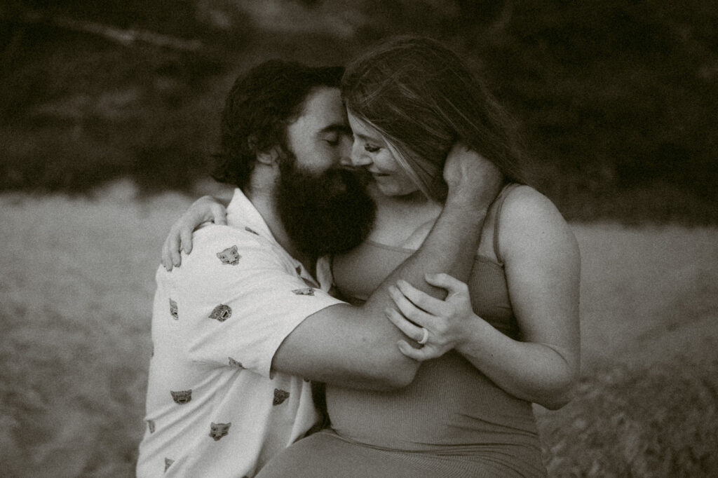 A black and white image of a young couple embracing on a log during their maternity session at Seal Rock Beach in Seal Rock, Oregon.