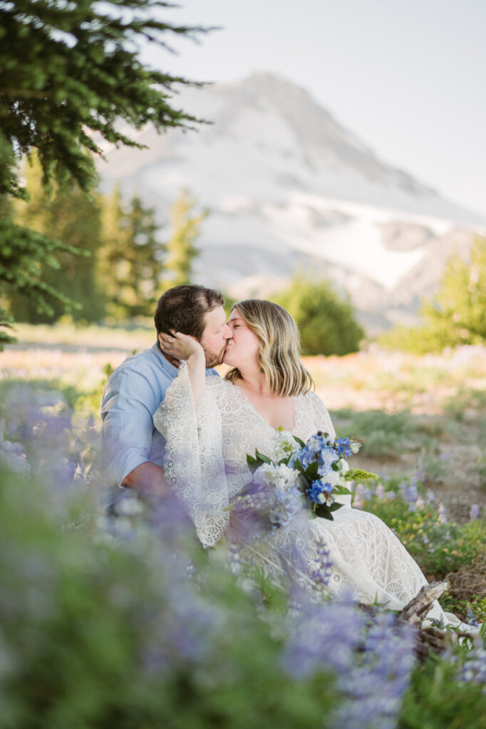 A bride and groom sit amongst a field of lupines during their elopement at Mount Hood Meadows. The summit of Mount Hood looms in the background.