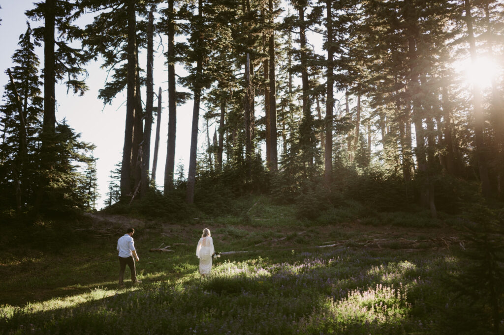 A bride and groom walk carefully through a field of lupines during their summer wedding at Mount Hood Meadows Ski Resort.