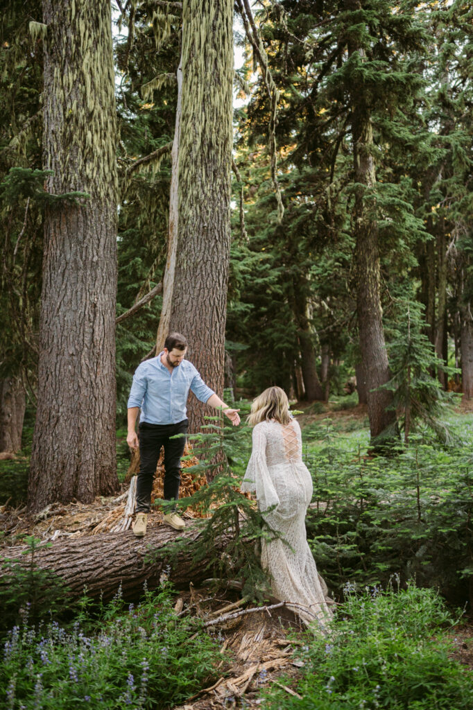 A groom helps his bride climb onto a fallen tree during their elopement at Mount Hood Meadows.