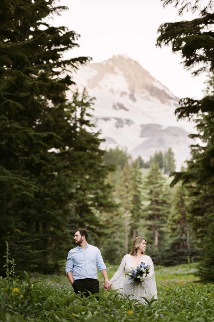 A bride and groom stand hand-in-hand and look opposite directions in a field of wildflowers during their summer wedding at Mount Hood Meadows Ski Resort.