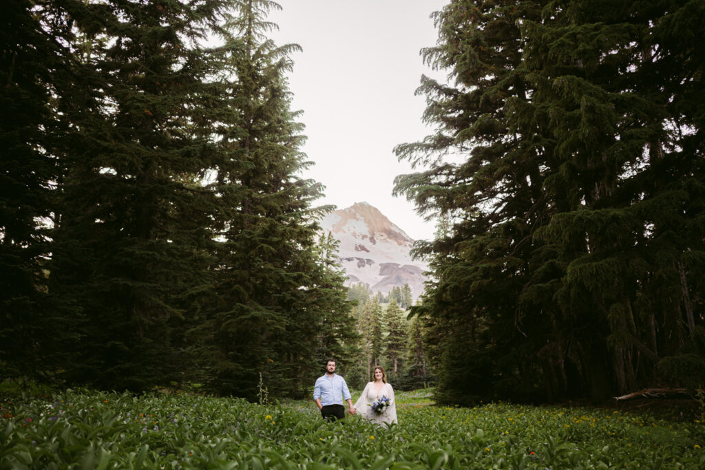 A bride and groom stand hand-in-hand in a field of wildflowers during their summer wedding at Mount Hood Meadows Ski Resort.