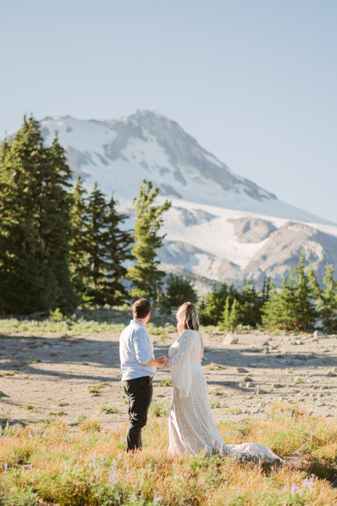 A bride and groom holding hands while looking at the summit of Mount Hood during their August wedding at Mount Hood Meadows