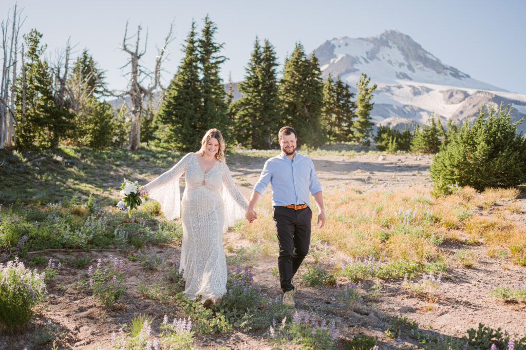 A bride and groom walk along the lupines and wildflowers during their adventure hiking elopement at Mount Hood Meadows