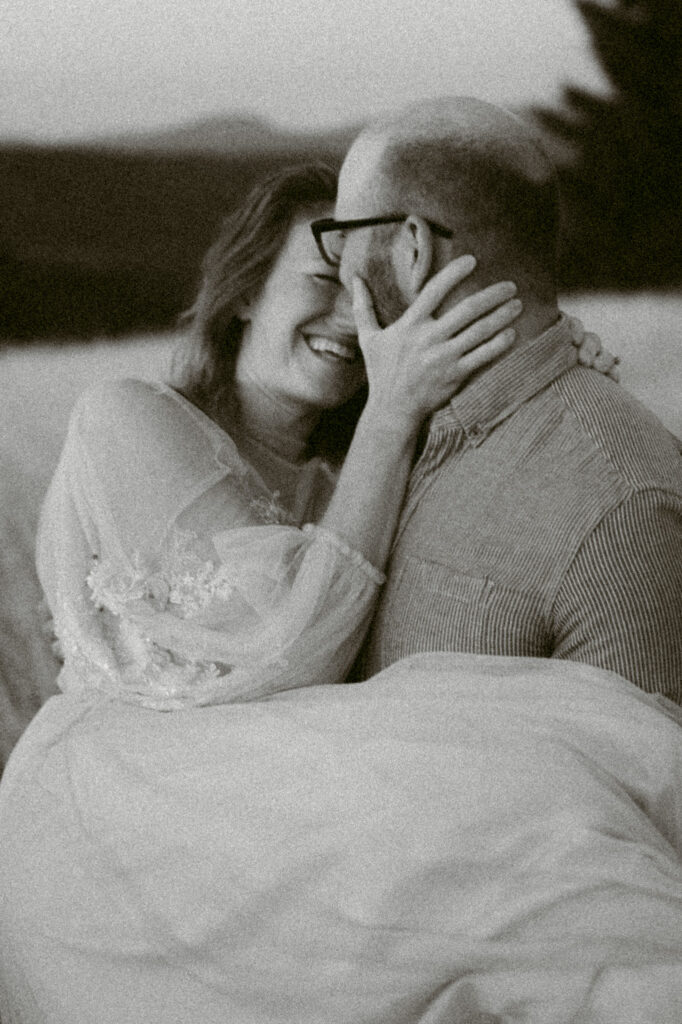 A close up black and white image of a woman laughing as she holds a man's face.