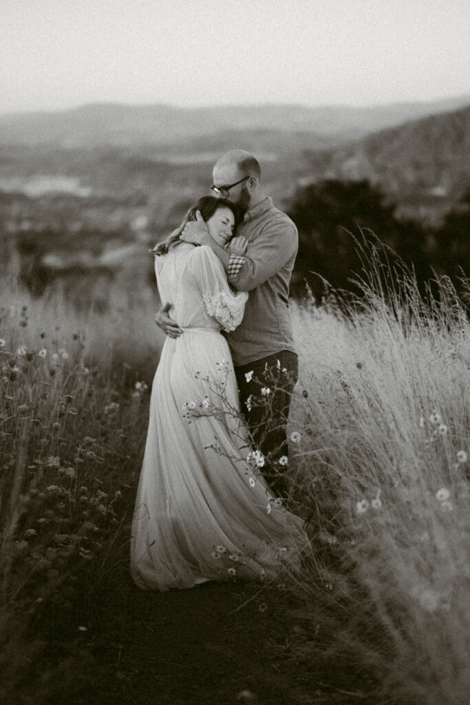 A black and white image of a man pulling a woman to his chest and kissing the top of her head during their anniversary session at Fitton Green in Corvallis, Oregon.