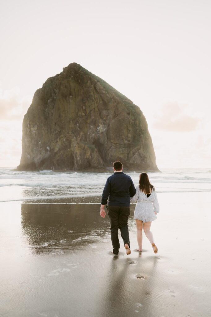 A young couple stroll hand-in-hand towards Haystack Rock at Cannon Beach in Oregon.