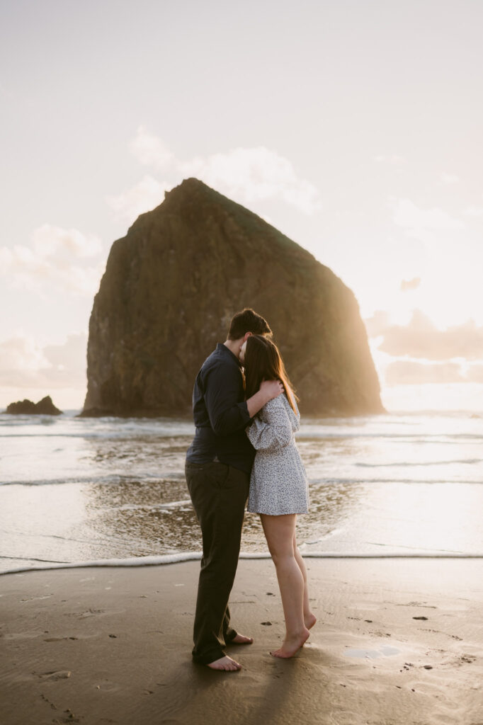 A young couple kisses in front of Haystack Rock at Cannon Beach during their sunset engagement session.