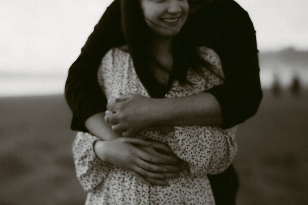 A black and white close-up image of a man's arms wrapped around a woman's torso.