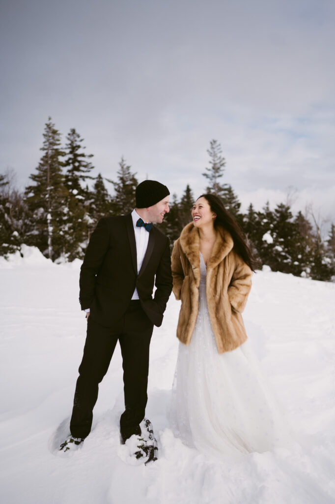 A bride and groom hold hands and smile at one another during their snowy winter elopement in the Adirondacks.