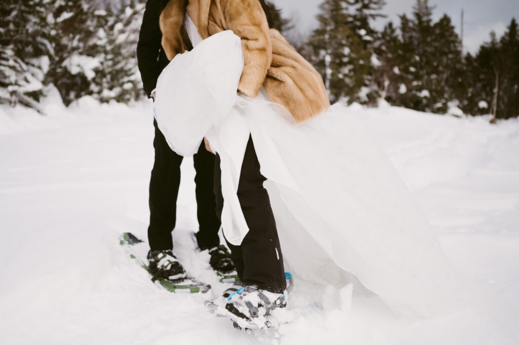 A bride lifts her train away from her snowshoes during her winter wedding in Lake Placid, NY.