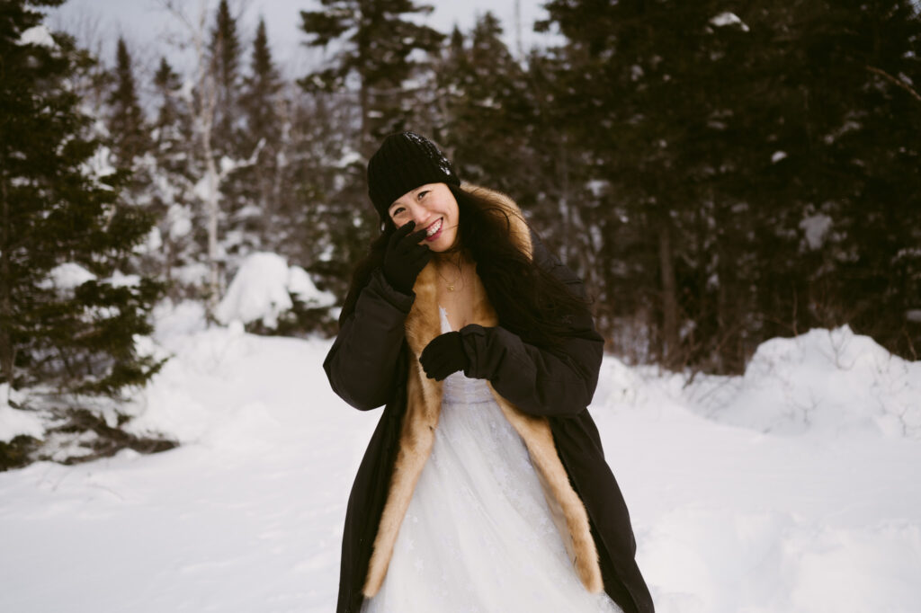 A bride smiles as she's bundled up for her winter hiking elopement in Lake Placid, New York.