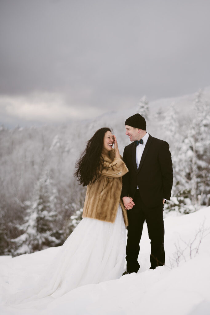 A bride and groom stand in a snowy mountain landscape during their winter Adirondack elopement in Lake Placid, NY.