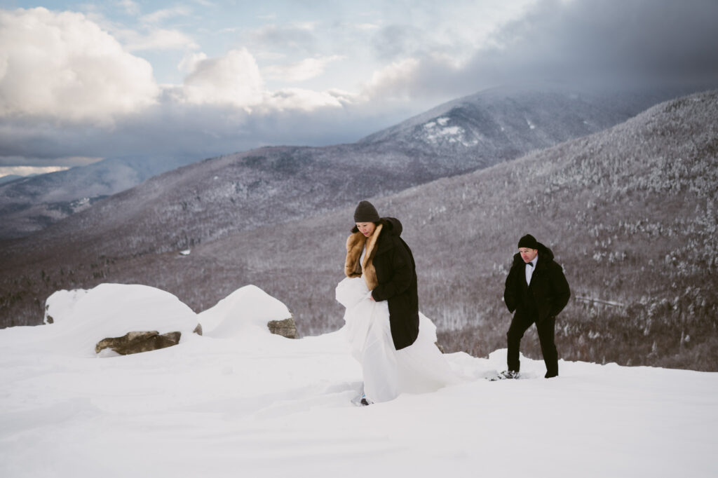 A bride and groom hike slowly through a winter landscape during their adventure elopement in Lake Placid, NY.