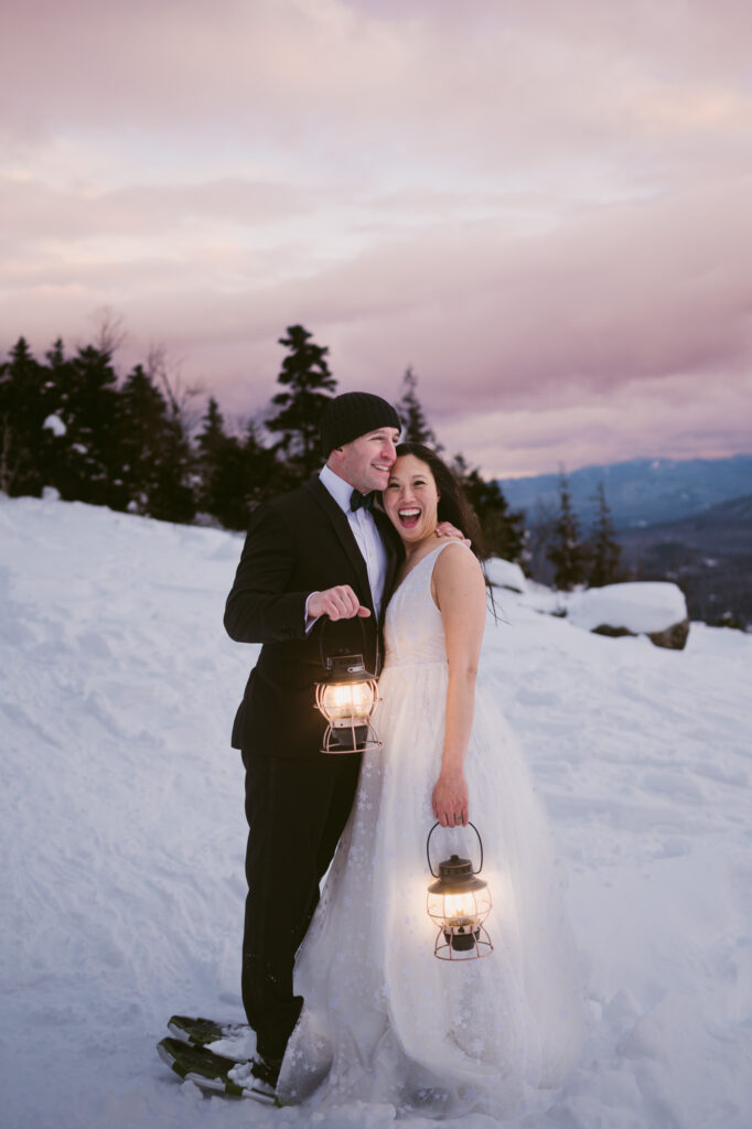 A bride and groom hold lanterns as the sun begins to set during their winter Adirondack elopement.