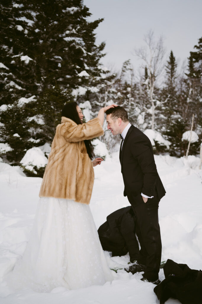 A bride fixes her groom's hair after they snowshoe hike to their winter elopement spot in Lake Placid, NY.